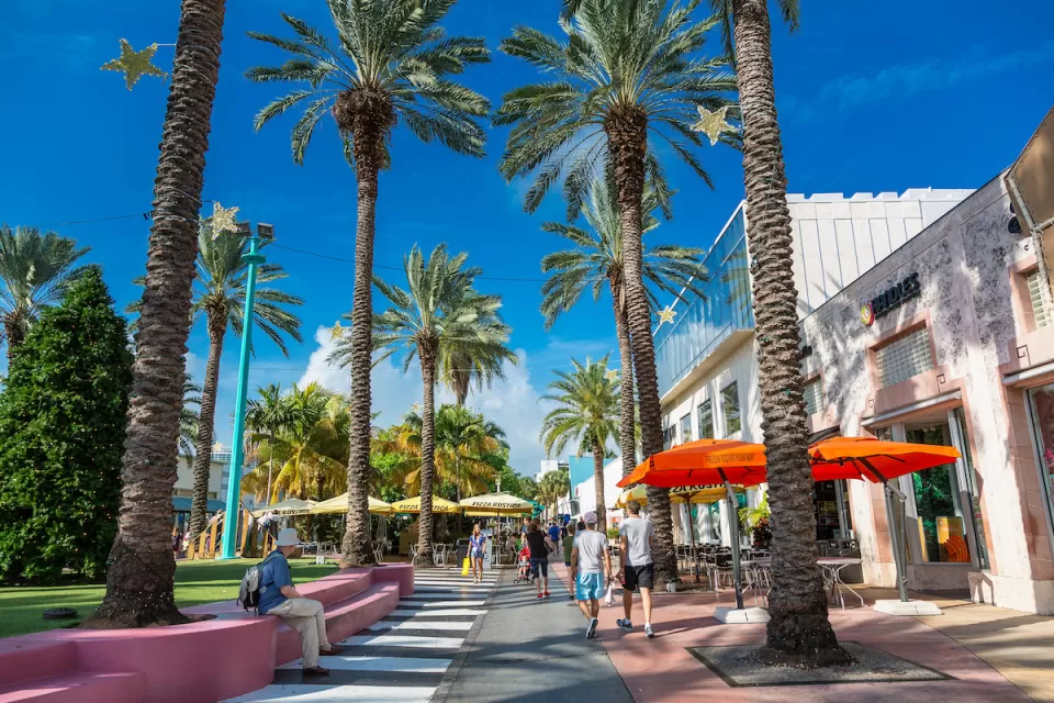 Pedestrian street with colorful patio umbrellas and tall palm trees in Miami, Florida.